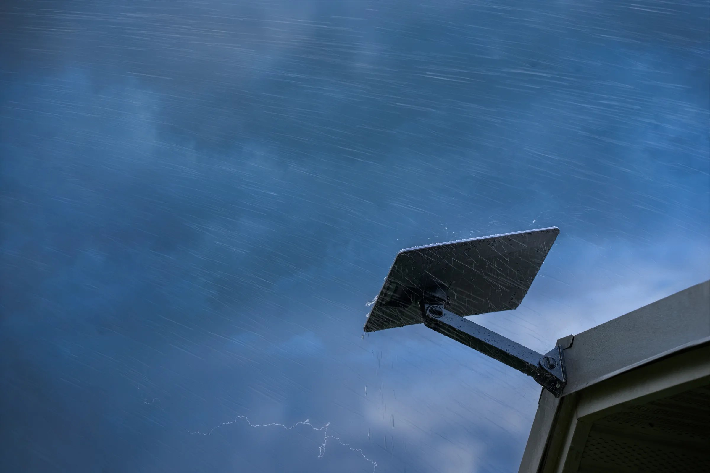 A Starlink dish on a rooftop in heavy rain, with lightning in the distance